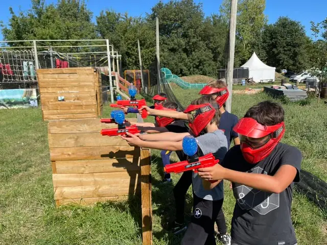 Des enfants visent derrière une barricade en bois, en extérieur